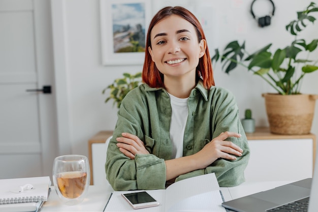 Foto retrato de uma jovem sorridente, trabalhando em casa com um laptop mulher de negócios relaxada com uma xícara de chá