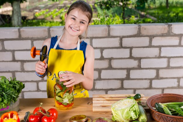 Retrato de uma jovem sorridente usando avental, preparando legumes frescos para preservação ou decapagem, em pé do lado de fora perto de um jardim segurando uma ferramenta para apertar a tampa