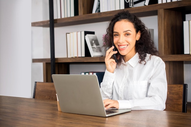 Retrato de uma jovem sorridente usando o telefone enquanto está sentada na mesa
