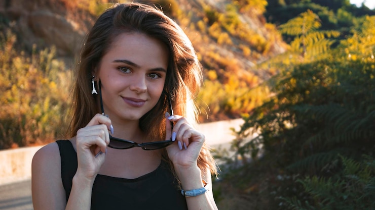 Foto retrato de uma jovem sorridente usando óculos de sol enquanto está de pé ao ar livre