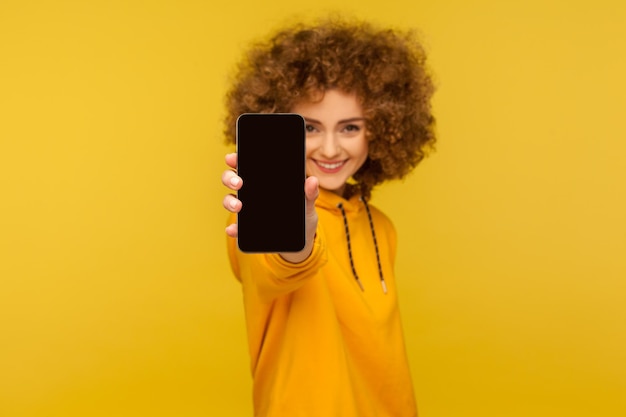 Foto retrato de uma jovem sorridente usando um smartphone contra um fundo amarelo