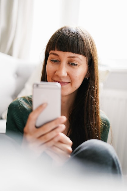 Retrato de uma jovem sorridente usando um telefone celular em casa