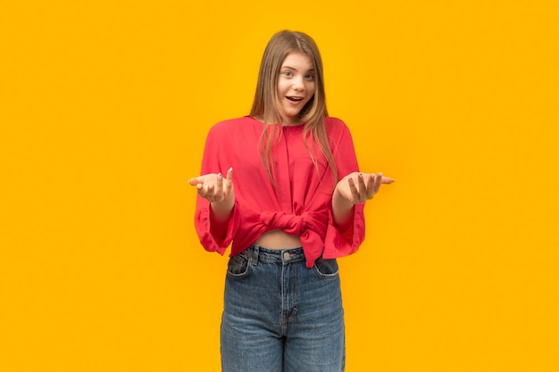 Retrato de uma jovem surpresa de pé com as palmas das mãos abertas isoladas em fundo amarelo jovem morena atônita