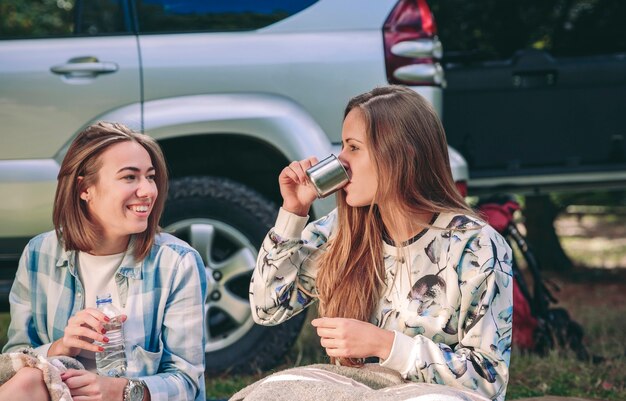 Retrato de uma jovem tomando uma xícara de café com uma amiga sentada sob o cobertor em um acampamento