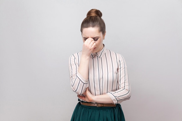 Retrato de uma jovem triste deprimida em camisa listrada e saia verde com penteado proibição coletados, em pé, segurando a cabeça baixa e chorando. tiro de estúdio interno, isolado em fundo cinza.