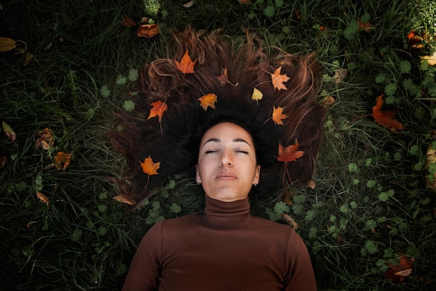 Retrato de uma jovem triste e bonita deitada no chão de uma floresta de outono com folhas de bordo coloridas Conceito segunda-feira azul