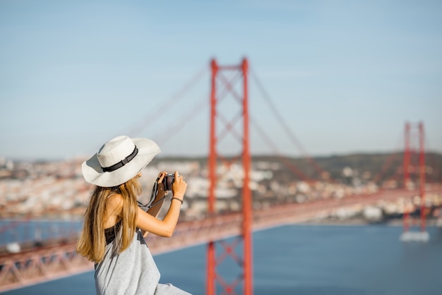 Retrato de uma jovem turista com uma câmera fotográfica sentada no fundo da paisagem com a bela ponte de ferro na cidade de Lisboa, Portugal