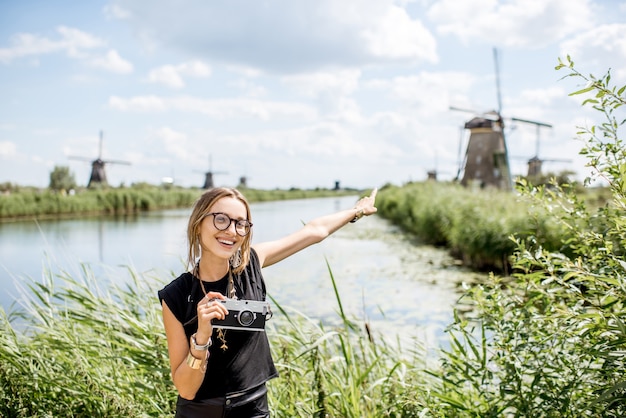 Retrato de uma jovem turista em pé com uma câmera fotográfica no fundo da bela paisagem com velhos moinhos de vento na holanda