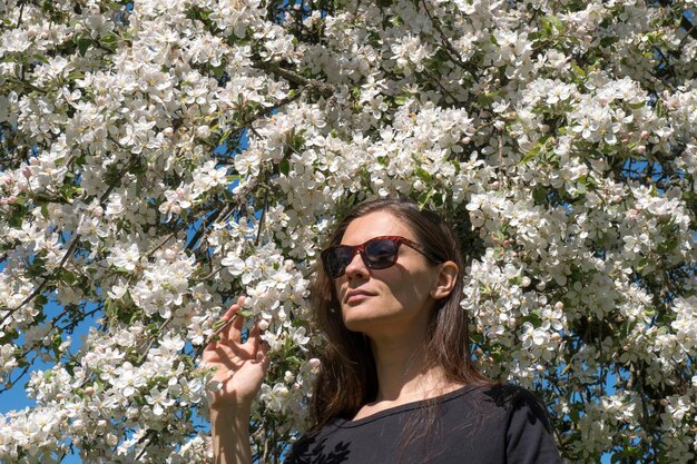 Foto retrato de uma jovem usando óculos de sol contra flores brancas de maçã