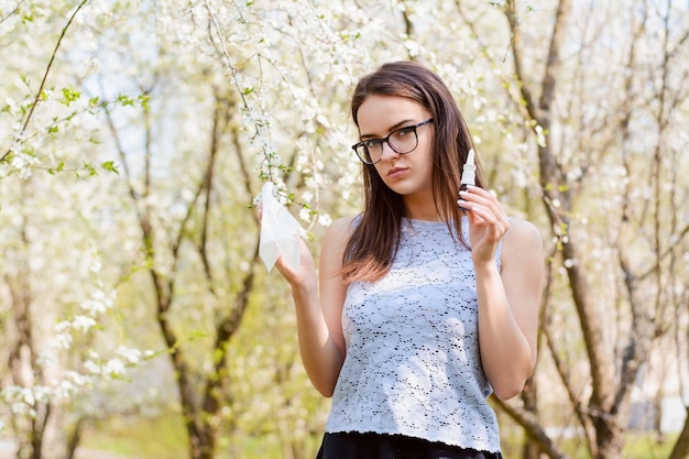 Retrato de uma jovem usando óculos e blusa leve, sofrendo de alergia ao pólen de flores