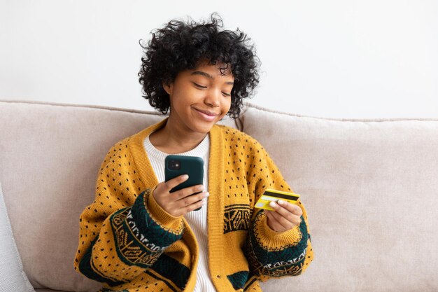 Foto retrato de uma jovem usando um telefone móvel enquanto está sentada no sofá em casa