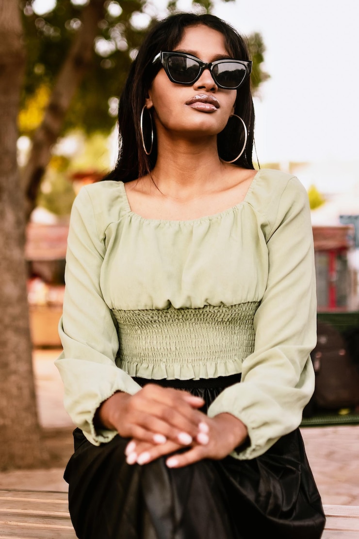 Foto retrato de uma jovem vestindo blusa verde claro, saia preta, óculos de sol e brincos de anel