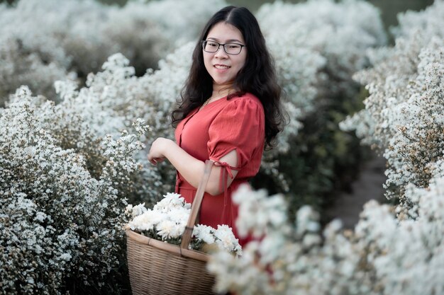 Retrato de uma jovem viajante feliz asiática com vestido vermelho, desfrutando de uma floração branca ou do campo de flores Margarida Marguerite branca para segurar uma cesta de flores no jardim natural de em Chiang Mai, Tailândia