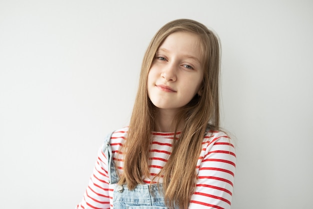 Retrato de uma linda adolescente com cabelo comprido, sorrindo em pé contra uma parede branca