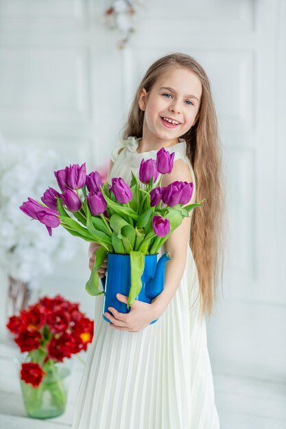 Retrato de uma linda criança de olhos azuis uma garotinha com um buquê de tulipas em uma sala brilhante