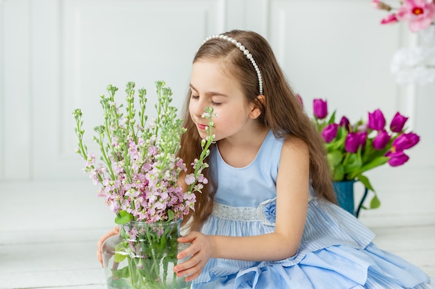 Retrato de uma linda criança de olhos azuis, uma menina com um buquê de tulipas em uma sala iluminada.