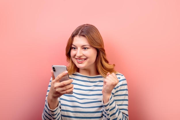 Retrato de uma linda e alegre garota de cabelos castanhos usando dispositivo de telefone 5g post como reação