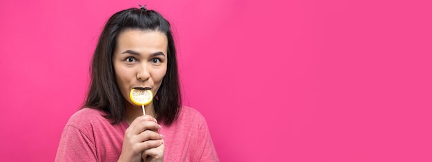 Retrato de uma linda e doce mulher alegre com cabelos castanhos lisos segurando um pirulito perto dos olhos