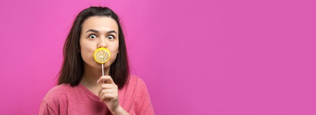 Retrato de uma linda e doce mulher alegre com cabelos castanhos lisos segurando um pirulito perto dos olhos