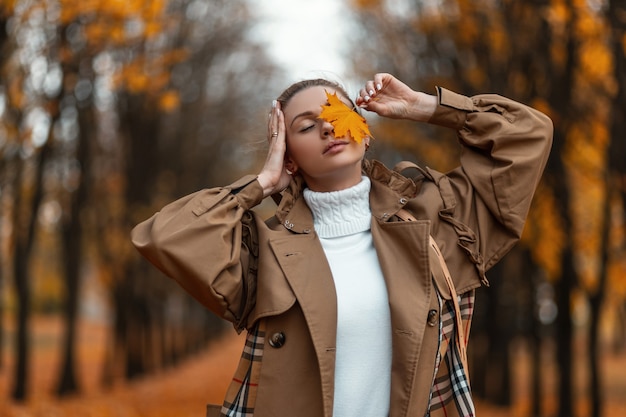 Foto retrato de uma linda e muito jovem mulher com roupas quentes elegantes e uma folha de bordo perto do rosto