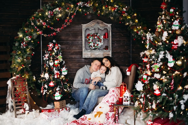 Retrato de uma linda família alegre em chapéus vermelhos e suéteres rindo e sorrindo na frente se abraçando contra a árvore de Natal decorada