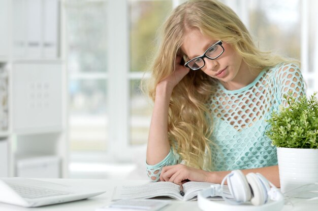 Retrato de uma linda garota adolescente sentada à mesa com o laptop e fazendo sua lição de casa