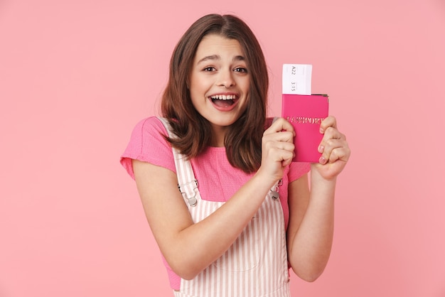 Foto retrato de uma linda garota animada usando piercing no nariz e segurando o passaporte com ingressos isolados na parede rosa