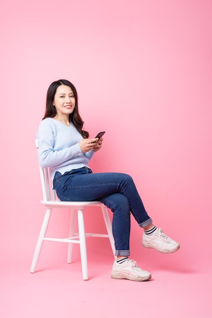 Retrato de uma linda garota asiática sentada na cadeira, isolada em um fundo rosa