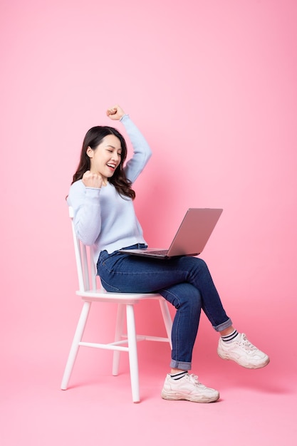 Retrato de uma linda garota asiática sentada na cadeira, isolada em um fundo rosa