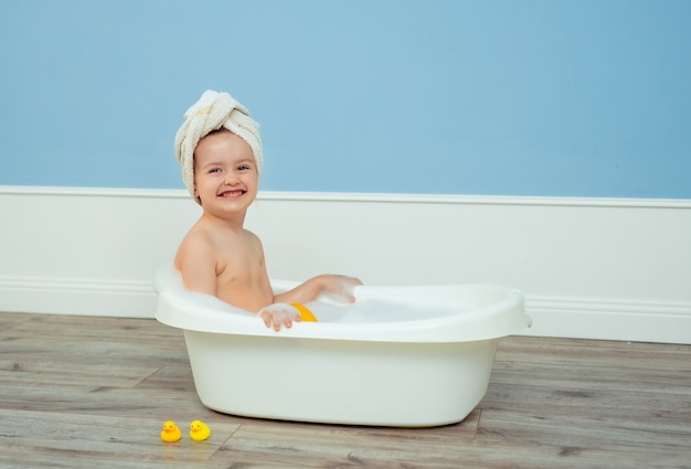 Retrato de uma linda garota bonita com uma toalha com um turbante na cabeça, que toma banho em um banho infantil com espuma e sabão.