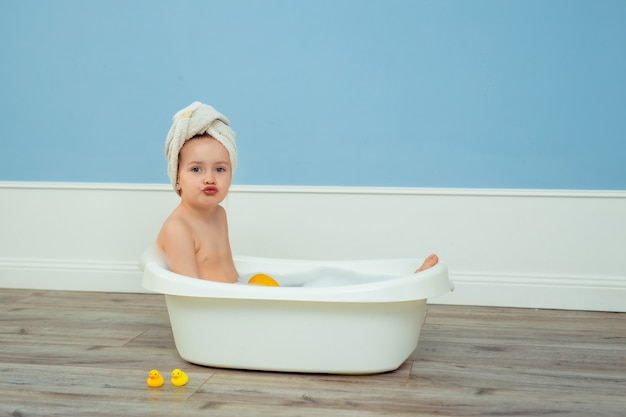 Retrato de uma linda garota bonita com uma toalha com um turbante na cabeça, que toma banho em um banho infantil com espuma e sabão.