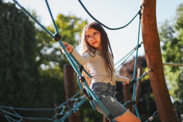 Retrato de uma linda garota caucasiana fica de lado em um balanço de corda em um parque em um playground