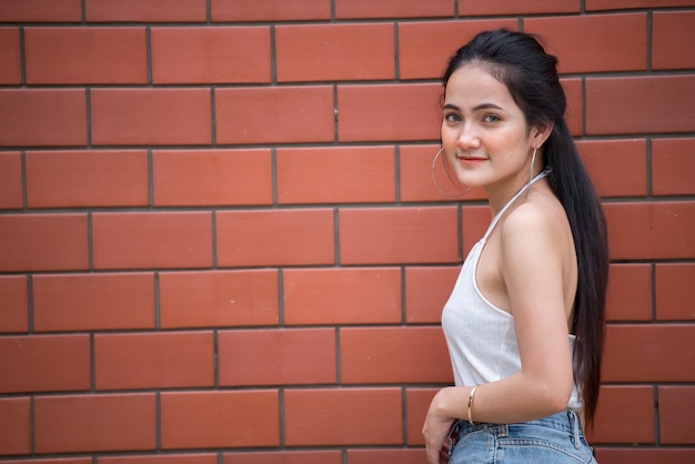 Retrato de uma linda garota chique asiática posar para tirar uma foto no fundo da parede de tijolosEstilo de vida do povo adolescente da Tailândia Conceito feliz de mulher modernaEstilo punk rock