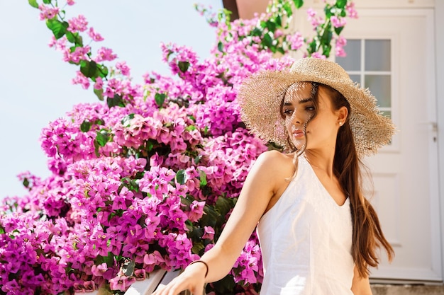 Retrato de uma linda garota com um chapéu perto de uma roseira florescendo.