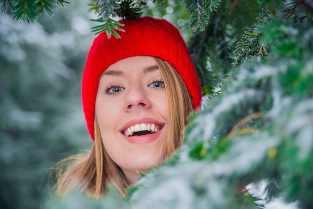 Retrato de uma linda garota com um chapéu vermelho. Feliz inverno. Bem vestido aproveitando o inverno. Menina brincando com neve no parque