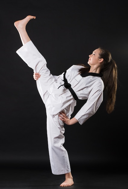 Foto retrato de uma linda garota de artes marciais em quimono exercitando karatê kata contra um fundo escuro