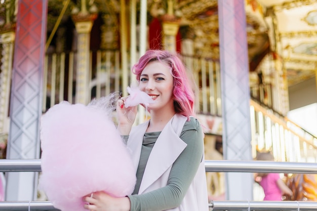 Retrato de uma linda garota de cabelo rosa com corte de cabelo curto, posando no parque de diversões no fundo do carrossel. Mulher com cabelo ombre rosa com lantejoulas cabelo fotodinâmico cachos brilhantes e brilhantes moda