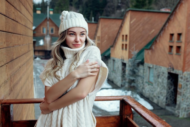 Retrato de uma linda garota de chapéu branco e suéter na rua na varanda Roupas quentes de inverno