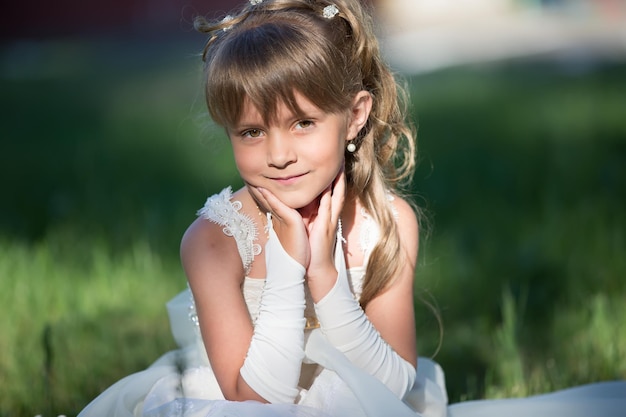 Retrato de uma linda garota de seis sete anos em um vestido branco na grama