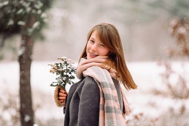 Retrato de uma linda garota em um clima gelado envolto em um lenço quente segurando um buquê com um sorriso