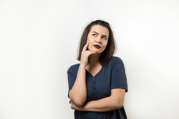 Retrato de uma linda garota em um fundo branco com pontos de interrogação parece de lado com expressão pensativa está considerando um plano para ação adicional