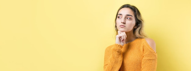 Retrato de uma linda garota em um suéter laranja olha de lado com expressão pensativa está considerando um plano para ação adicional