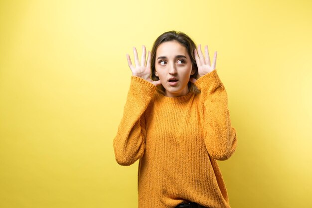 Retrato de uma linda garota em um suéter laranja olha de lado com expressão pensativa está considerando um plano para ação adicional