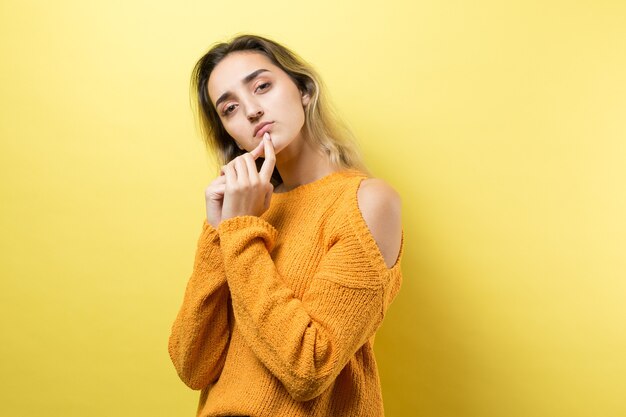 Retrato de uma linda garota em um suéter laranja olhando de lado com expressão pensativa
