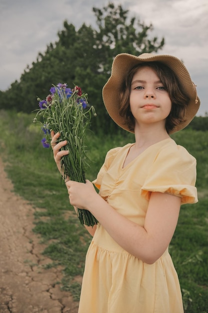 retrato de uma linda garota em um vestido amarelo e chapéu com um buquê de flores no campo