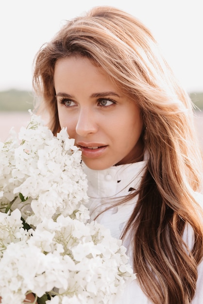 Retrato de uma linda garota em um vestido branco com um buquê de flores em um campo no verão