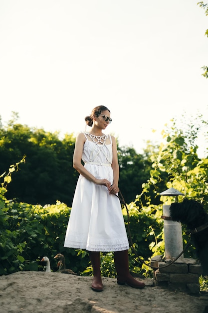 Foto retrato de uma linda garota em um vestido branco no jardim burnette linda garota natural com um vestido branco na natureza na rua no jardim por uma árvore com maquiagem e penteado