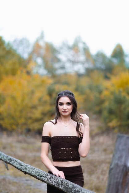 Retrato de uma linda garota em um vestido de malha marrom Uma garota posa em um fundo de campo verde e céu branco