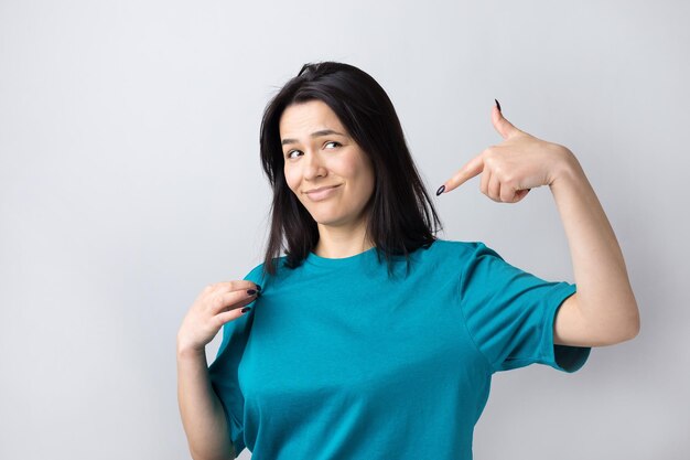 Retrato de uma linda garota em uma camiseta azul olha de lado com expressão pensativa está considerando um plano para ação adicional