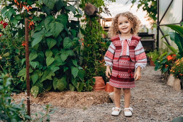 Retrato de uma linda garota encaracolada vestida com vestido bordado folclórico ucraniano posando para uma foto no jardim com flores